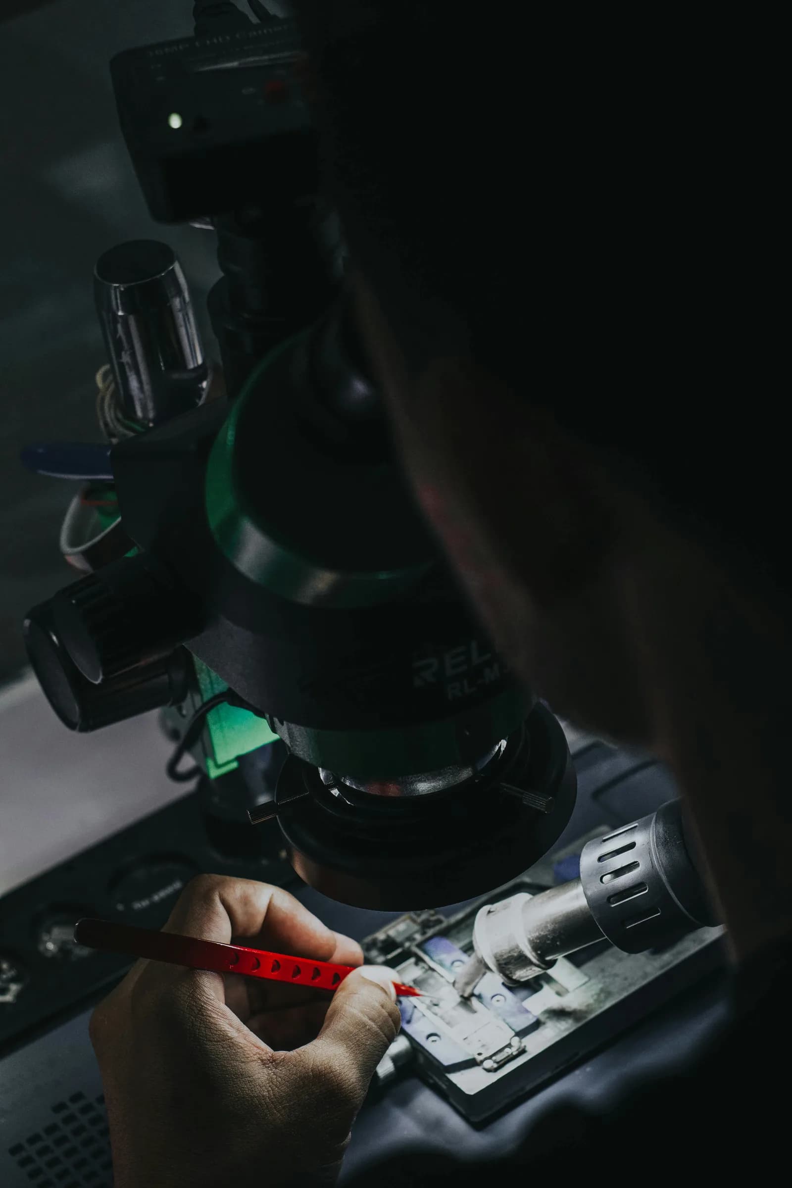 Technician working on a logic board with a microscope, tweezers and a hot-air tool